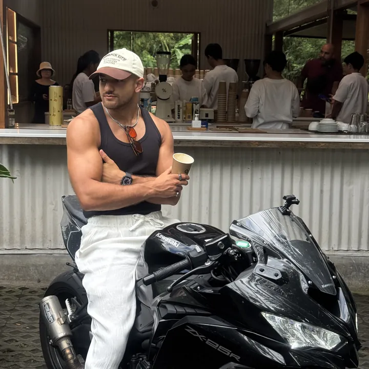 Anwar on a motorbike with a coffee outside a cafe in Bali