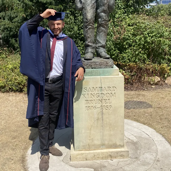 Anwar in his graduation gown beside the Brunel statue